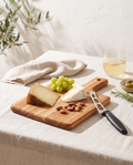 Tabla de teca con cuchillo para queso y tabla de quesos en una mesa de verano