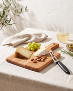 Tabla de teca con cuchillo para queso y tabla de quesos en una mesa de verano